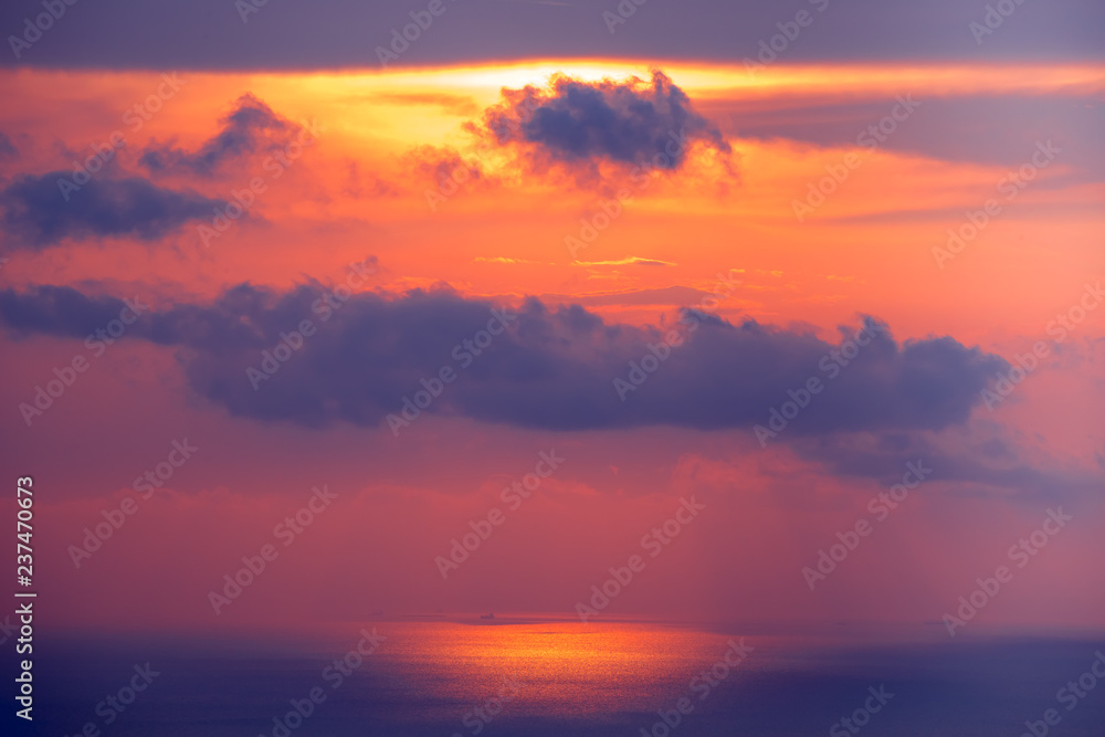 Sunset cloudy sky over ocean water. Amazing landscape in bright scarlet, blue tints. Bright sky with dense clouds over water surface. Sun lights reflection. Beauty of wild untouched nature.