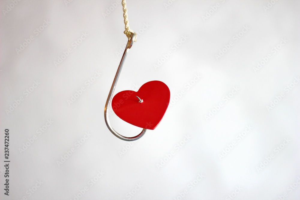 A metal fishing hook hanging on a rope pierced the red cardboard heart. Bad heart.. A metal fishing hook hanging on a rope pierced the red cardboard heart. Bad heart..