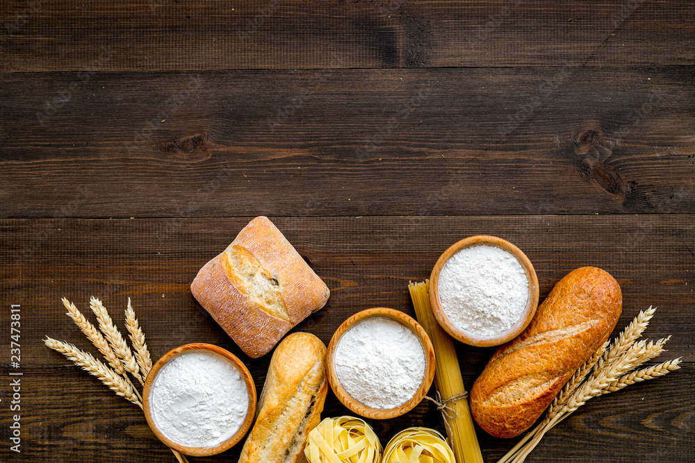 Bakery production, making bread and pasta. Fresh bread and raw pasta near flour in bowl and wheat ears on dark wooden background top view copy space