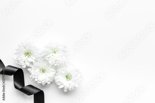 Funeral symbols. White flower near black ribbon on white background top view copy space