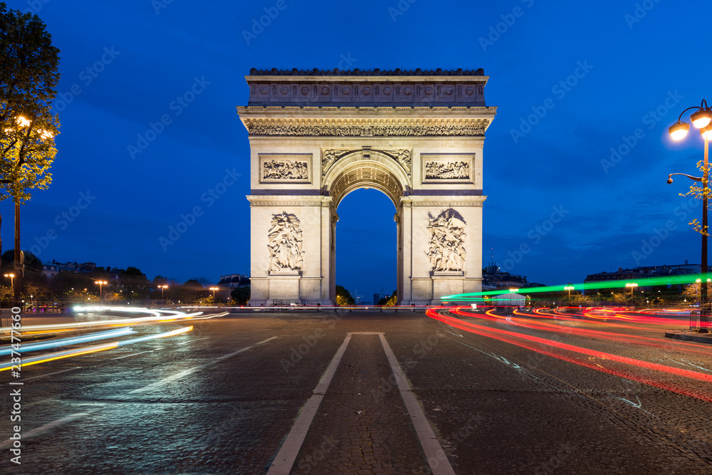 Paris street at night with the Arc de Triomphe in Paris, France.