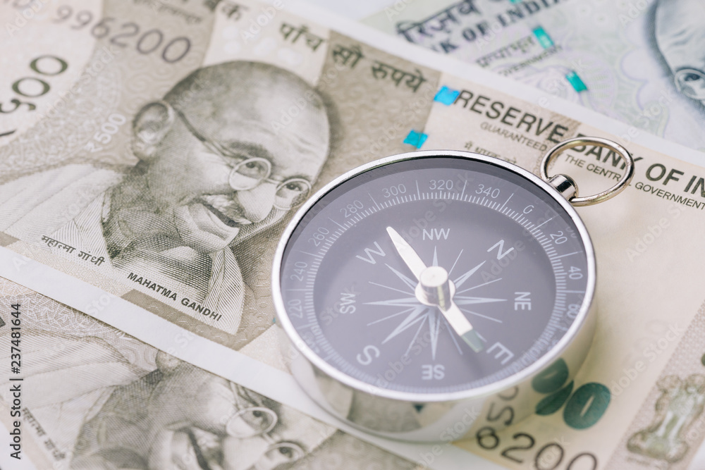 Direction of india financial and economy, new asia developing and emerging market high growth country concept, closed up of compass on indian rupee banknotes on table Direction of india financial and economy, new asia developing and emerging market high growth country concept, closed up of compass on indian rupee banknotes on table