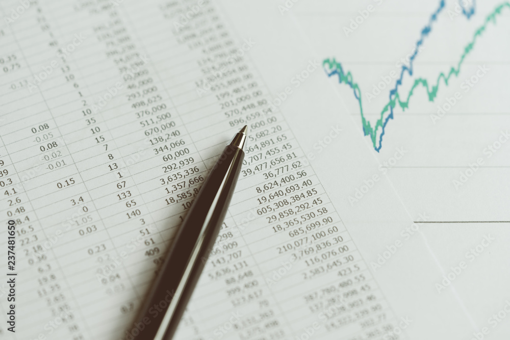 Fototapeta premium Investment, financial report statistic concept, close-up of black pen on printed stock exchange data price number or valuation table with green and blue yearly graph