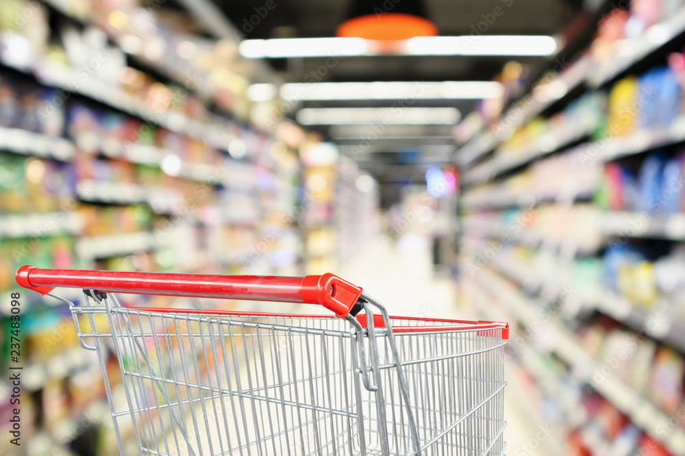Supermarket aisle blurred background with empty red shopping cart