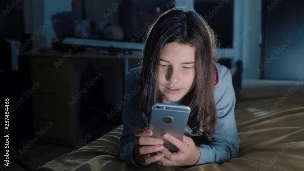girl teenager and smartphone. little teen hood girl writes a message chatting in social media messenger night evening indoors smartphone on the bed. children technology and communication concept girl teenager and smartphone. little teen hood girl writes a message chatting in social media messenger night evening indoors smartphone on the bed. children technology and communication concept