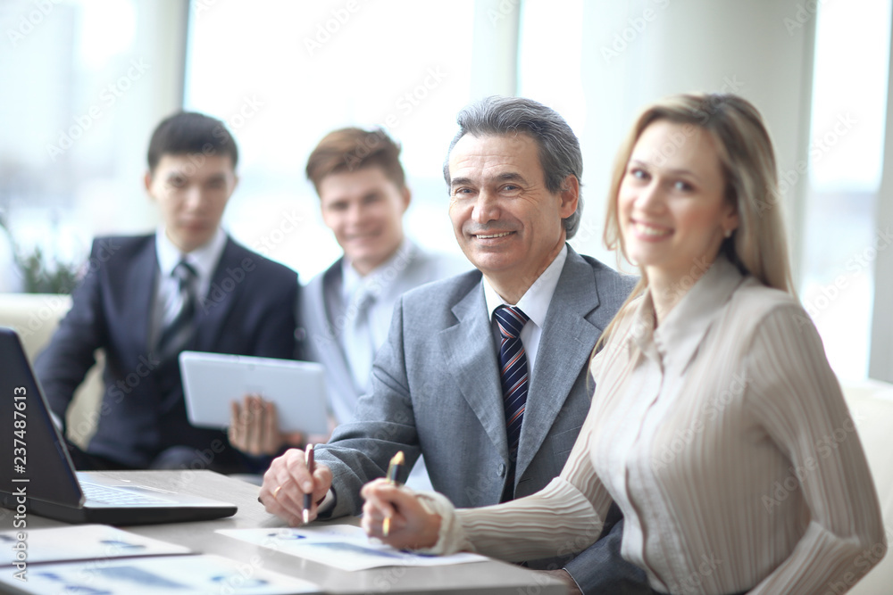 Portrait of mature business man smiling during meeting with colleagues in background Portrait of mature business man smiling during meeting with colleagues in background