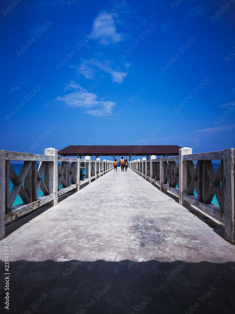 Wooden jetty in the noon under clear blue skies with people walking.
