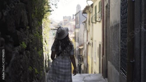 Young woman walking on history centre european city. Following from the back girl in dark on narrow street between buildings wall. Porto, Portugal