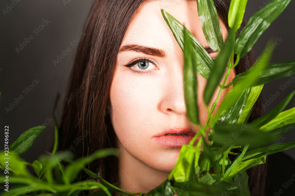 Beauty portrait of a brunette in a dark vein. Woman face and leaf of tropical palm. Beauty portrait of a brunette in a dark vein. Woman face and leaf of tropical palm.