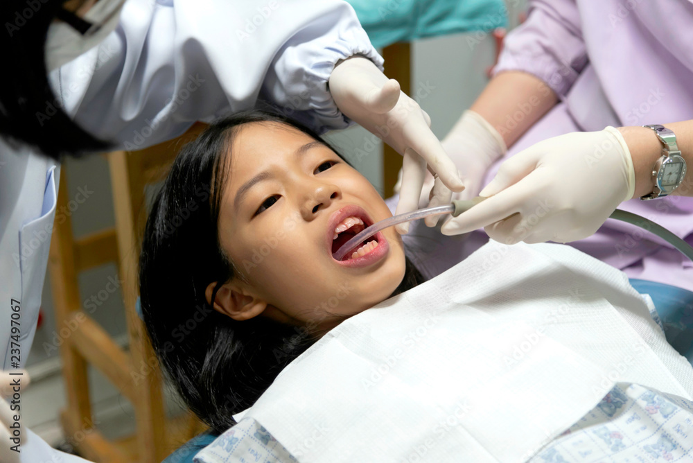 Close up of young Asian Pre teen girl having dental professional treatment in stomatology clinic. Kid patient at dental office open mouth with suction. Dentist examining and cleaning her teeth. Close up of young Asian Pre teen girl having dental professional treatment in stomatology clinic. Kid patient at dental office open mouth with suction. Dentist examining and cleaning her teeth.