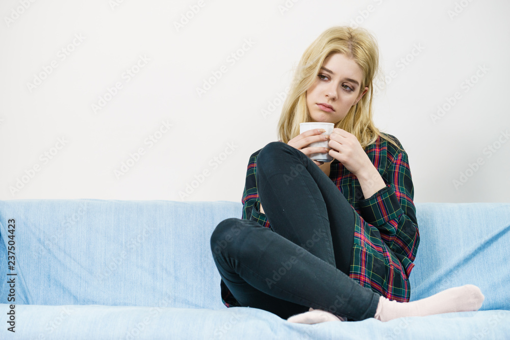 Sad lonely woman sitting on couch with mug Sad lonely woman sitting on couch with mug