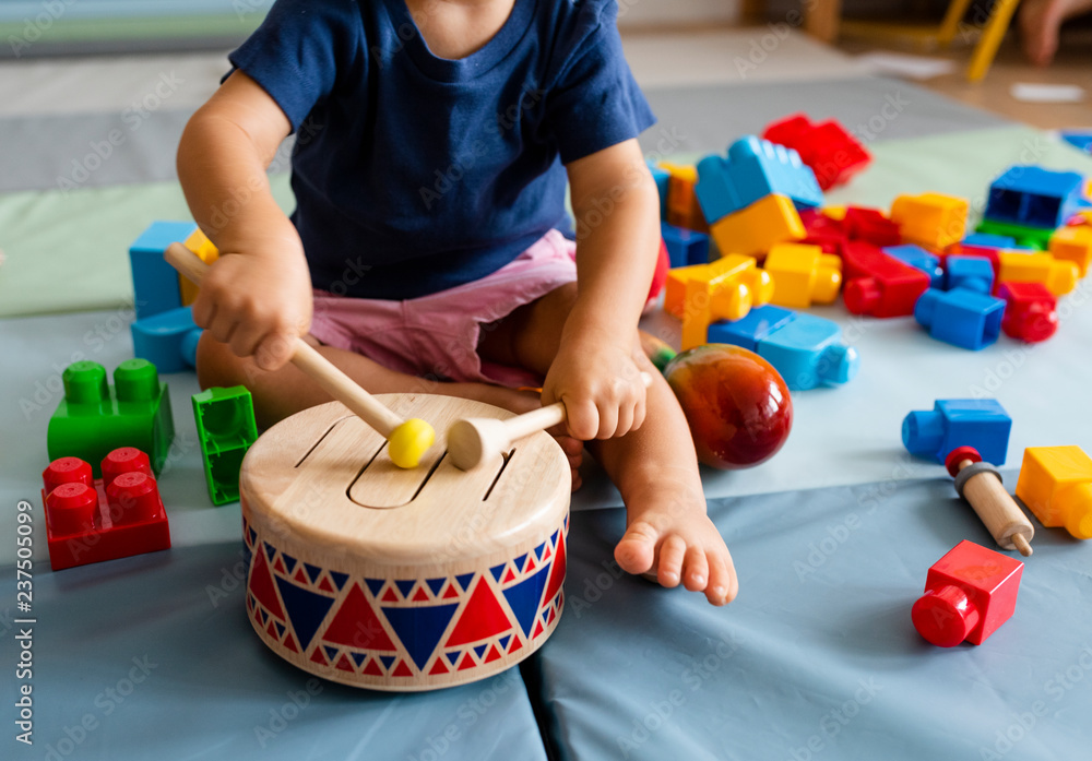 Little boy having fun and playing wooden toy drum - obrazy, fototapety, plakaty 
