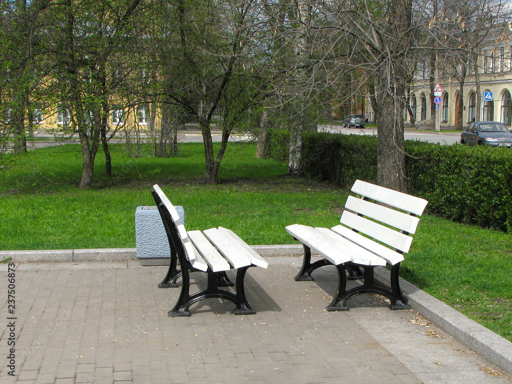 Two white benches stand opposite each other in the park. Benches for friends.