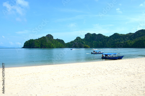 Andaman Sea coast on the island of Langkawi, Malaysia. Small boats near the shore and in the sea. White clouds and white sand
