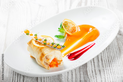 Fish rolls with vegetables, cheese and orange sauce on wooden background. Hot fish dish. Top view