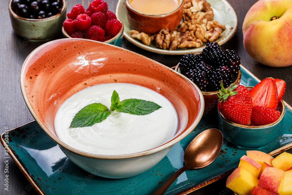 Yogurt with topping of currants, blackberries, strawberries, peaches, raspberries, nuts and honey on dark wooden background close up. Fresh yogurt. Healthy breakfast. Top view Yogurt with topping of currants, blackberries, strawberries, peaches, raspberries, nuts and honey on dark wooden background close up. Fresh yogurt. Healthy breakfast. Top view