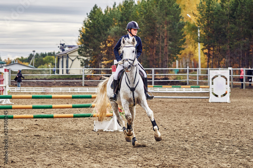 Young woman jockey in white blue dress and black boots, takes part in equestrian competitions.