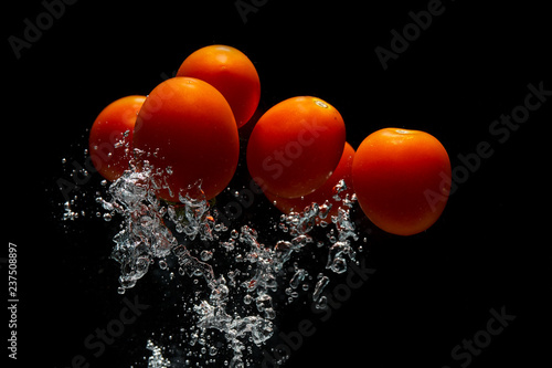 Red tomato on black background with water splash