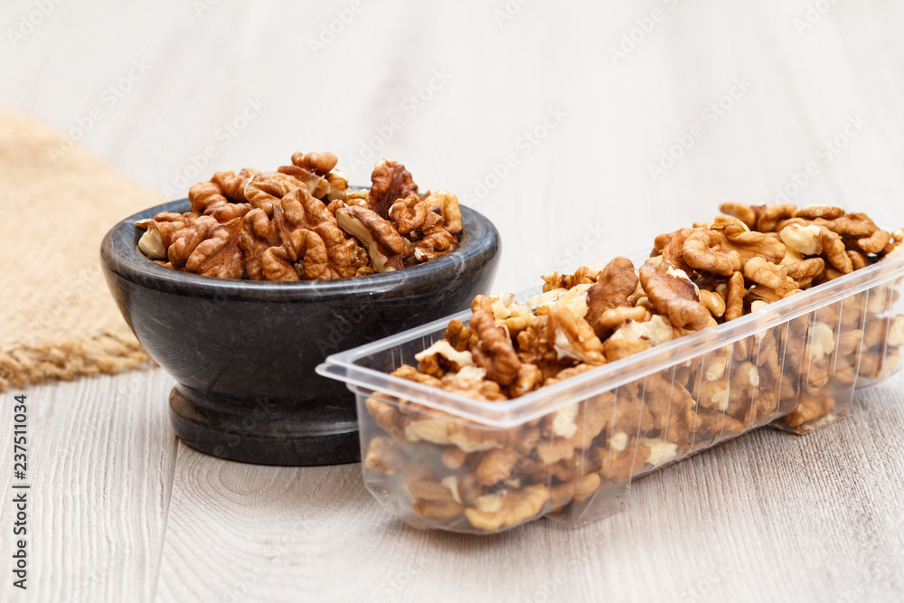Walnuts in stone bowl and plastic container on a wooden background. Walnuts in stone bowl and plastic container on a wooden background.
