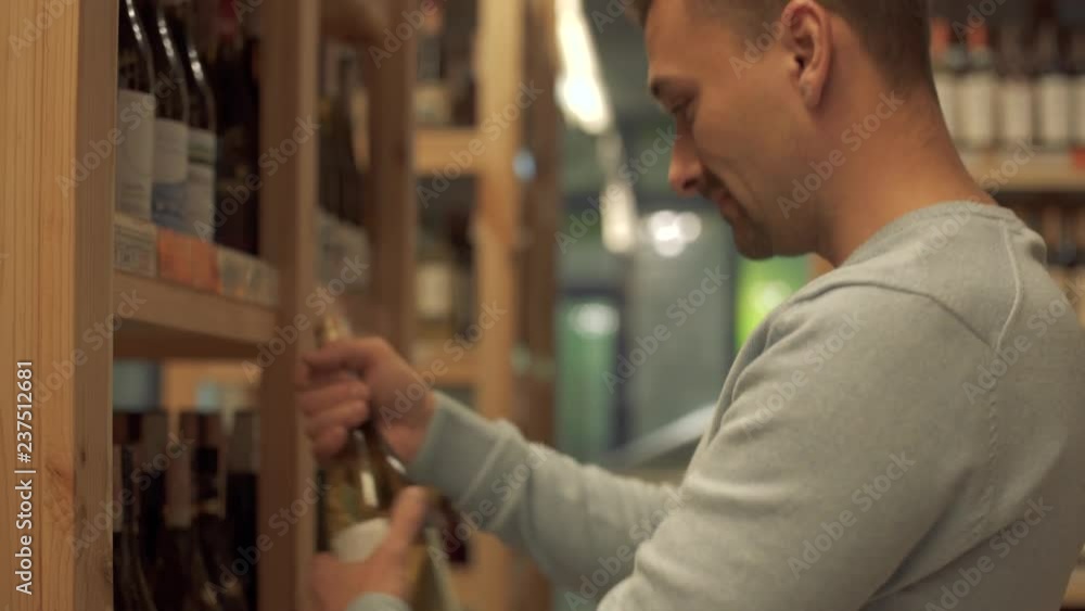 Portrait of cheerful man is taking white wine bottle in the shop close up Customer is choosing drink in alcohol shop Portrait of cheerful man is taking white wine bottle in the shop close up Customer is choosing drink in alcohol shop