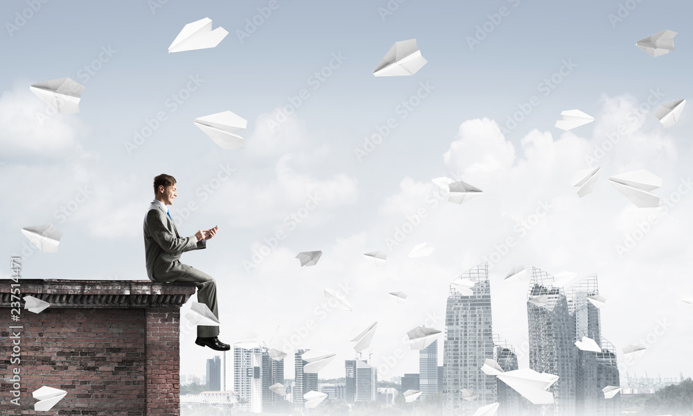 Businessman or student on roof edge making calls and cityscape at background Businessman or student on roof edge making calls and cityscape at background