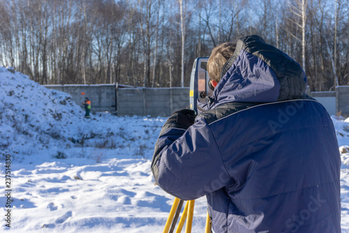 A surveyor with an assistant makes a topographical survey for the cadastre at a construction site in winter photo