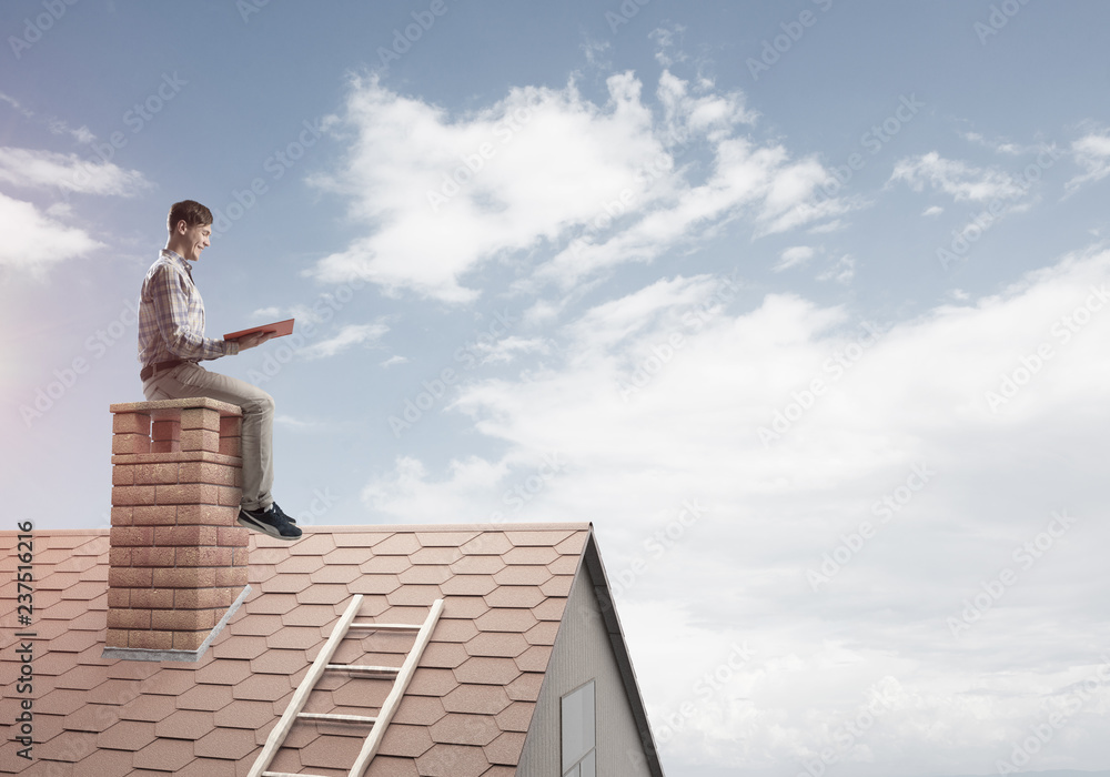 Handsome man on brick roof against cloud scape reading book