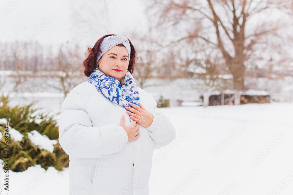 Holidays days, Christmas winter time. Plus size Woman in coat and headband outdoor. Lady in casual clothes, plump lady fashion concept, posing on the street in snowy weather 