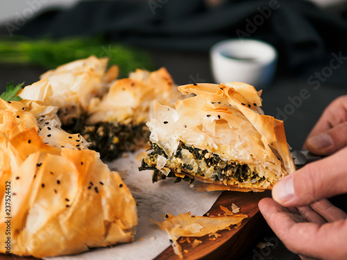Slice of greek pie spanakopita in hand. Ideas and recipes for vegetarian or vegan Spanakopita Spinach Pie from fillo pastry cut in slices. Copy space. Side view photo