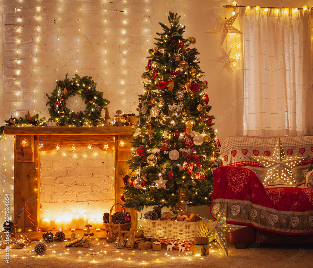 Christmas living room interior, decorated wood mantelpiece, lit up tree with red gold green baubles and ornaments, stars, wreath, candles, lightly toned, cosy chair with red cover, selective focus