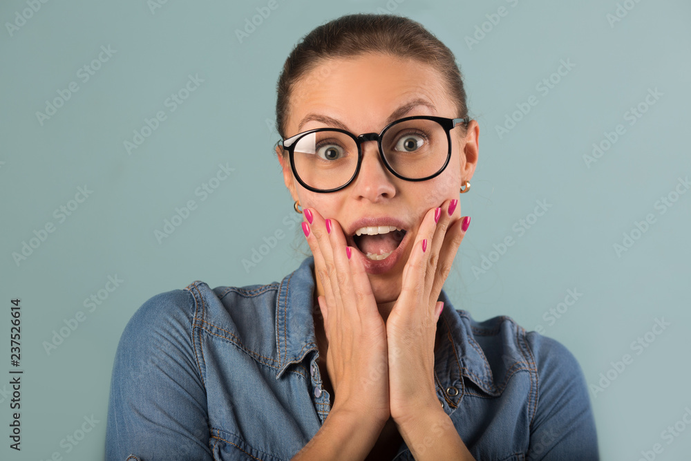 beautiful young girl in a denim shirt with glasses on a blue background with astonishment on her face beautiful young girl in a denim shirt with glasses on a blue background with astonishment on her face