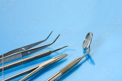 Dentist tools: mirror, explorer, tweezers and kornzange or forceps on blue glass background.