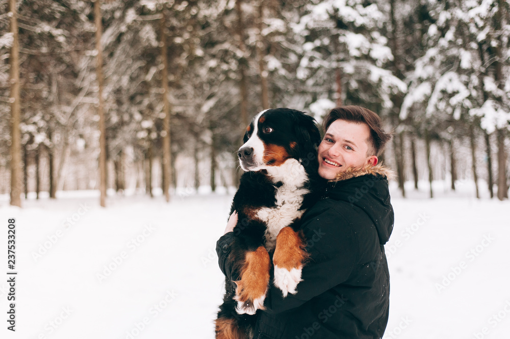 young man in the winter forest with  berner dog