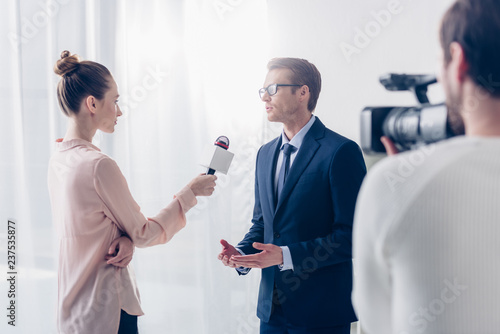 handsome businessman in glasses giving video interview to beautiful journalist in office