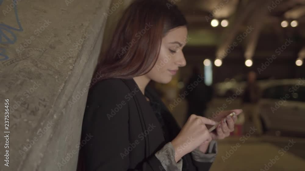 Brunette young woman using smartphone in night city. Female teleworker with gadget outdoors, panning shot. Using gadget concept Brunette young woman using smartphone in night city. Female teleworker with gadget outdoors, panning shot. Using gadget concept