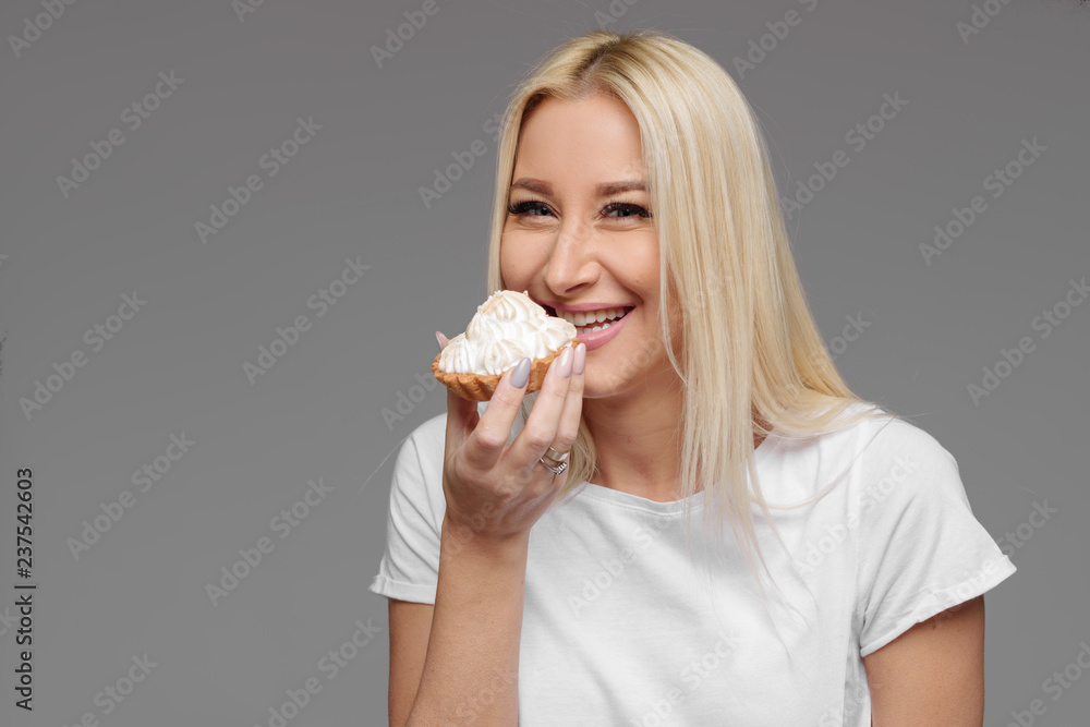 Laughing blond woman eating cake isolated on a grey background. No diet Laughing blond woman eating cake isolated on a grey background. No diet