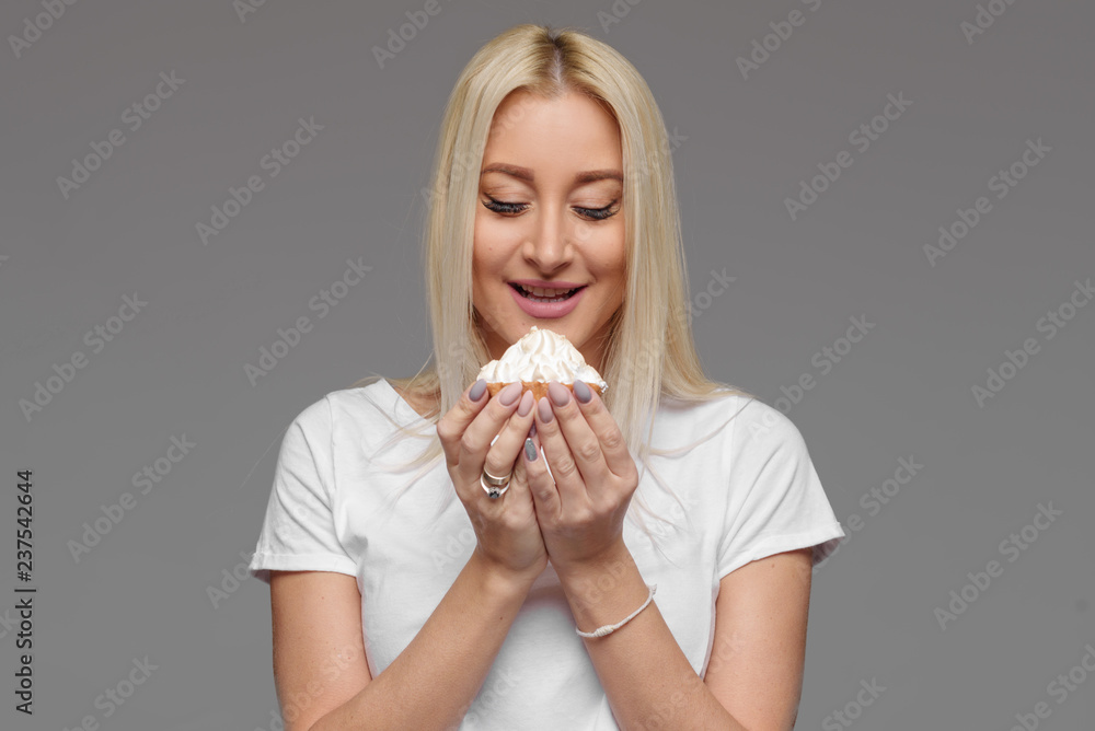 Laughing blond woman eating cake isolated on a grey background. No diet Laughing blond woman eating cake isolated on a grey background. No diet