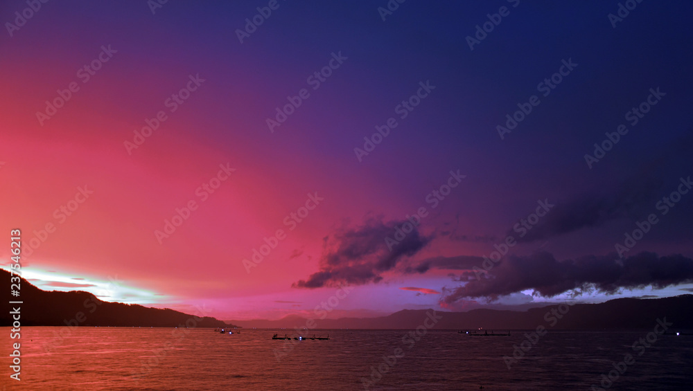 Very beautiful purple sunset in Lake Toba, Sumatra, Indonesia. Clouds and mountains in the background. Fishing traps in the lake.