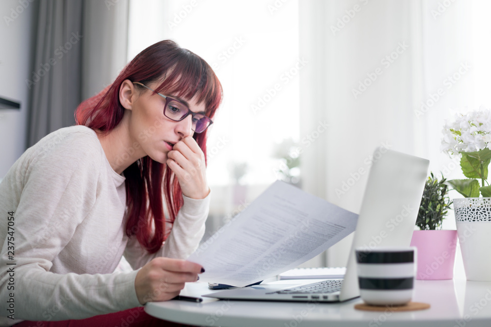 Worried woman at home checking financial documents using calculator and laptop Worried woman at home checking financial documents using calculator and laptop