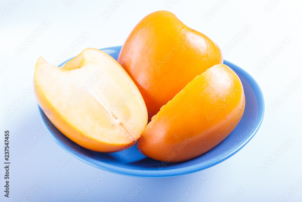 Ripe orange persimmon in a blue plate isolated on white background.