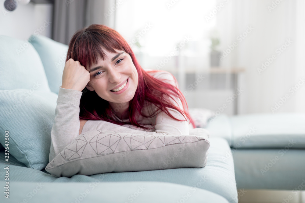 Woman with friendly smile looking at camera while lying on sofa in living room Woman with friendly smile looking at camera while lying on sofa in living room