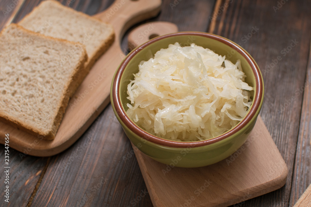 Sauerkraut in a plate and a piece of bread on a wooden background. Sauerkraut in a plate and a piece of bread on a wooden background.