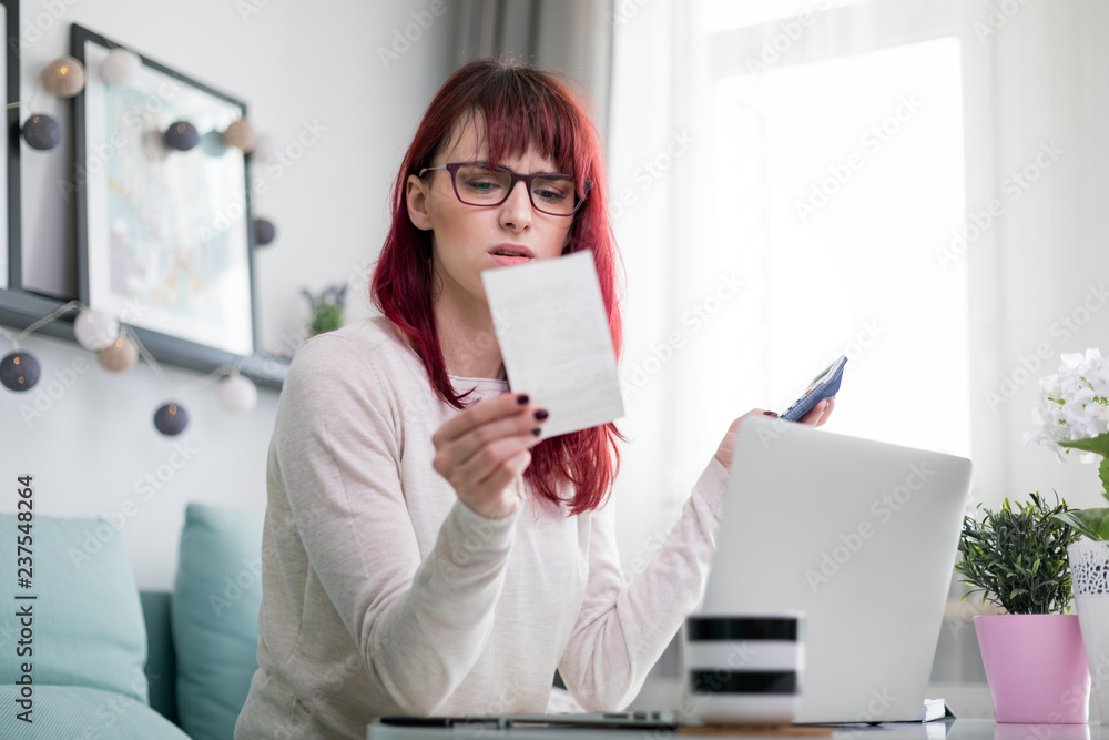 Stressed shocked woman at home checking financial documents using calculator and laptop Stressed shocked woman at home checking financial documents using calculator and laptop