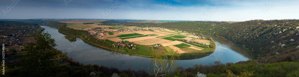 View of the village in spring from a bird's eye view. Panoramic photo of a beautiful village and fields on a peninsula surrounded by a river in the spring season.