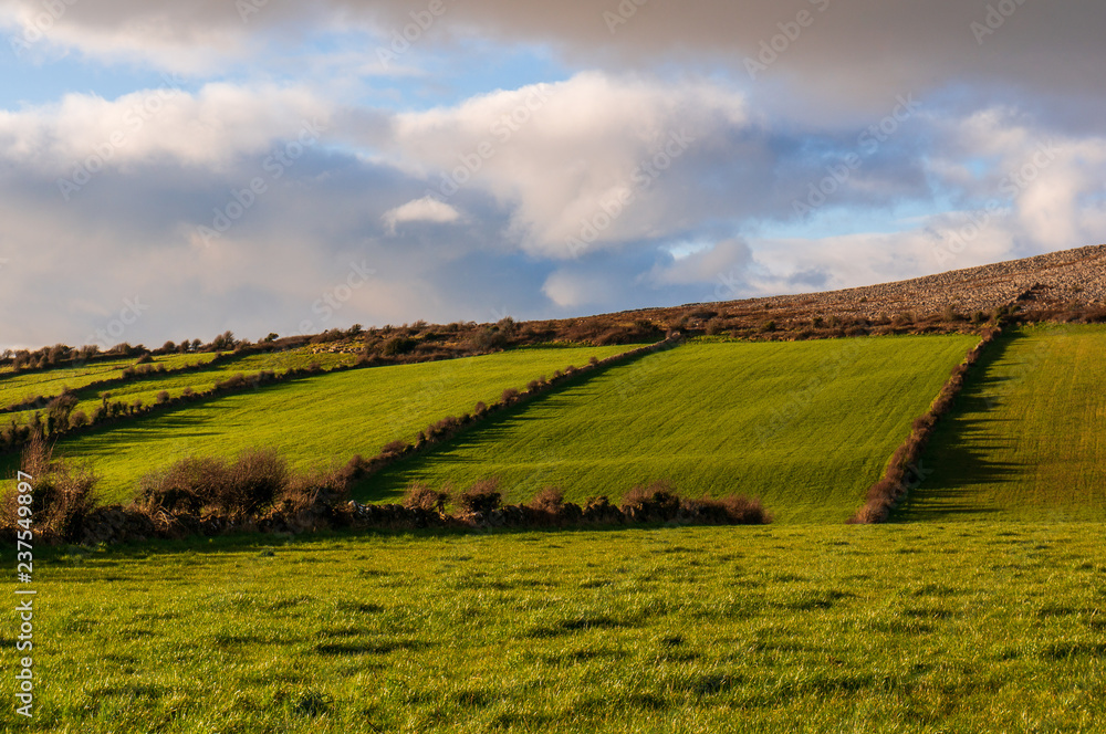 Beautiful Irish landscape with green grass covered hills in the middle of the winter. Typical countryside scenery in Ireland under a dramatic sky.