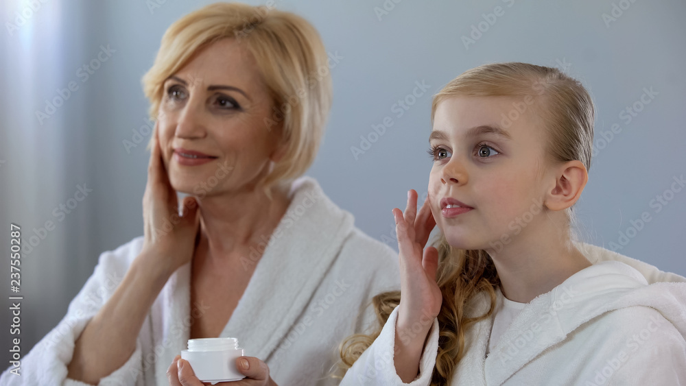 Pretty grandmother and granddaughter applying face cream and smiling, skin care Pretty grandmother and granddaughter applying face cream and smiling, skin care