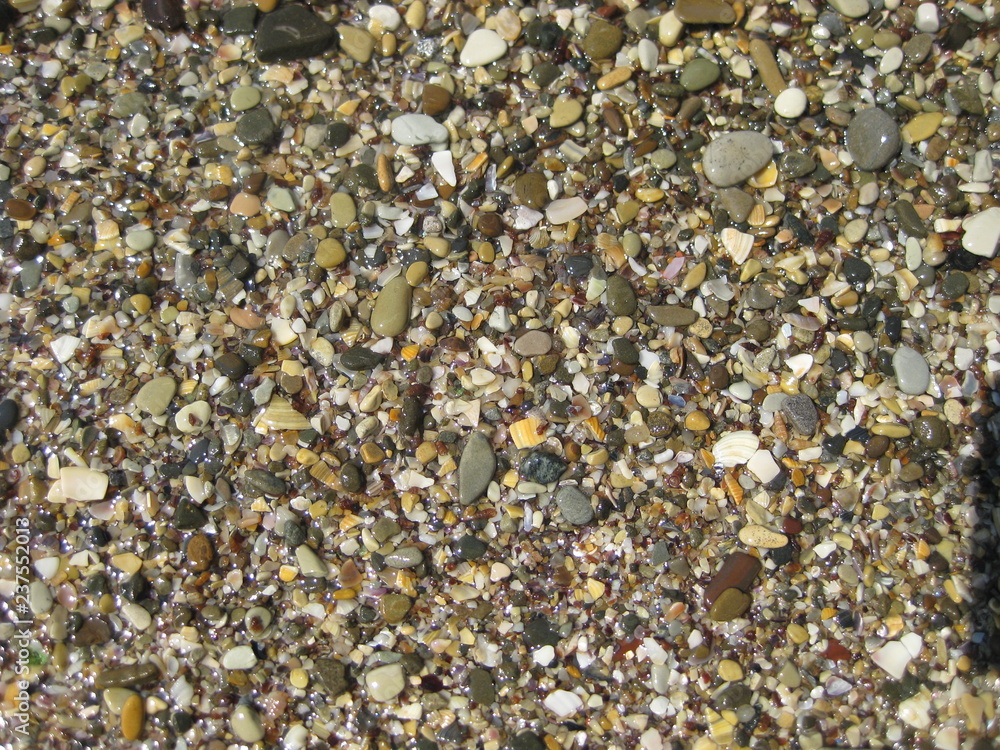 Small stones on the beach. Pebbles-stones lying on the beach, right by the water. Colorful stones are wet and shiny in the sun. Small stones on the beach. Pebbles-stones lying on the beach, right by the water. Colorful stones are wet and shiny in the sun.