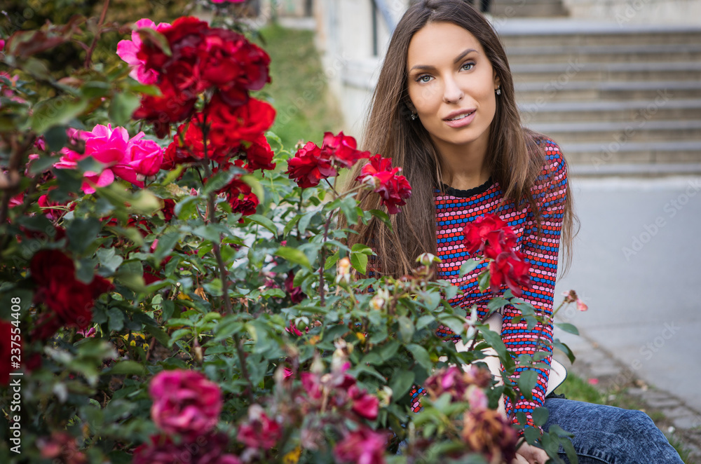Portrait of beautiful young girl near flower bed of roses.