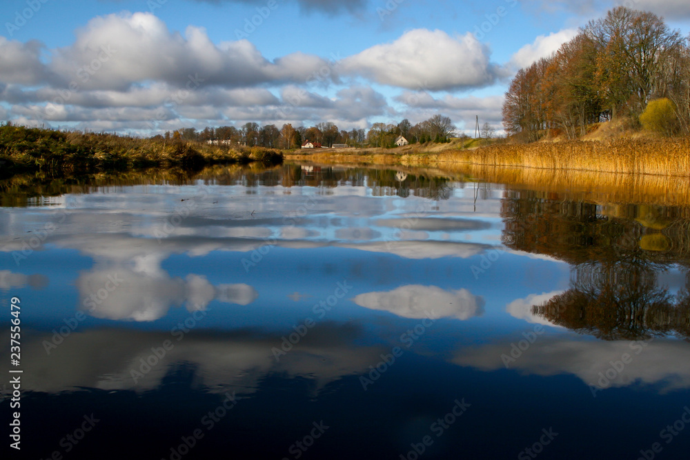Autumn landscape with colorful trees, yellow grass and river. Reflection in river Autumn landscape with colorful trees, yellow grass and river. Reflection in river