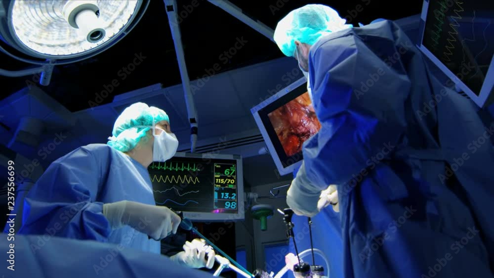 Medical European Caucasian surgical team in scrubs performing Laparoscopy surgery on the patient in operating theatre using video camera technology 
